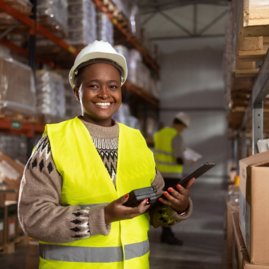 African American woman in a yellow vest and white hard hat in the factory working