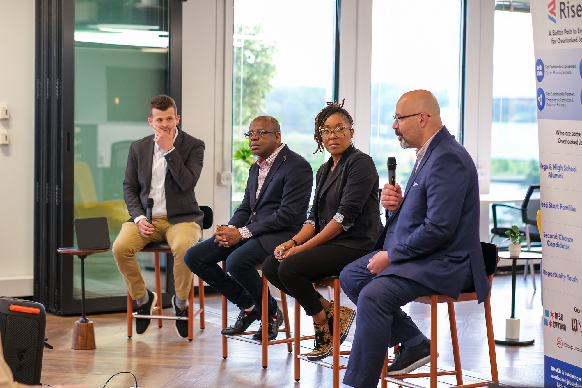 4 people sitting on stools as panelists speaking