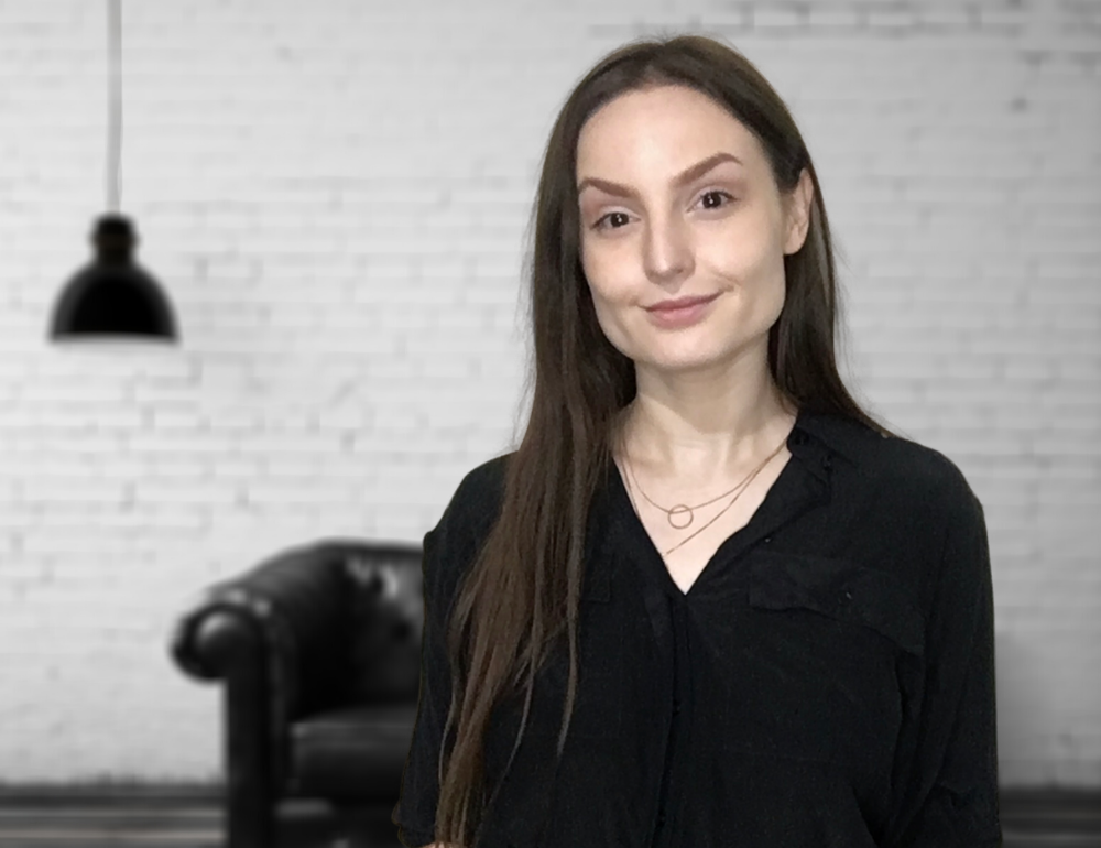 Kelly Schairer, Caucasian woman with brown hair in front on a white brick background.