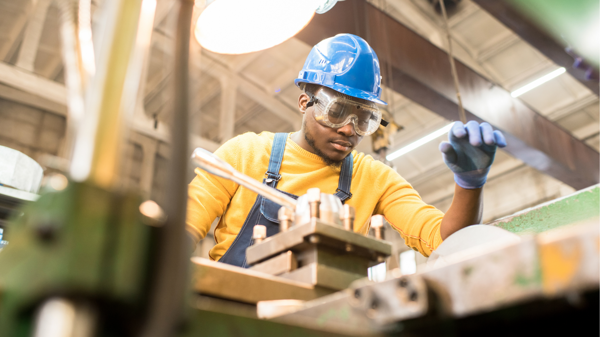 Manufacturing worker in a blue hard hat, yellow shirt with blue overalls in a factory working